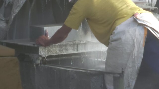 A worker adjusting a heavy stone block on a wet cutting saw machine in a workshop