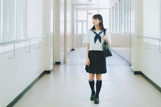 学校の廊下を歩く夏服の女子高校生
