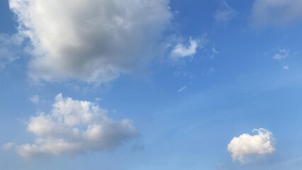 Obraz premium Bright blue sky background with small isolated white clouds