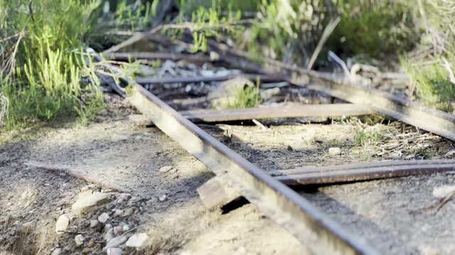 Old rusty abandoned narrow-gauge mine railway tracks overgrown