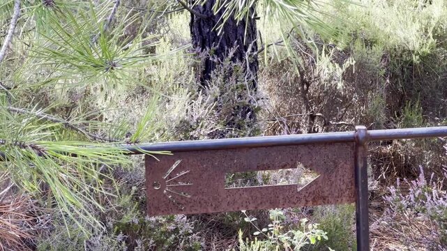 Panning view of a rusty metal trail signpost with a cut-out scallop
