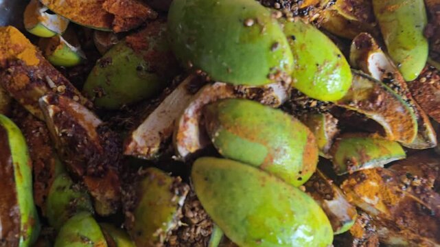 Traditional green mango pickle preparation, raw mango slices mixed with aromatic Indian spices, spicy homemade mango achar with oil and chili