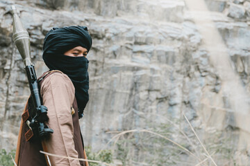 Fototapeta premium Outdoor military concept. Masked person with rocket launcher near rocky cliff in outdoor wilderness setting