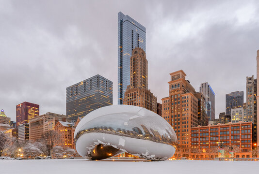 Cloud Gate ("The Bean") covered in fresh snow during winter in Millennium Park, with the downtown Chicago skyline rising behind the iconic public sculpture