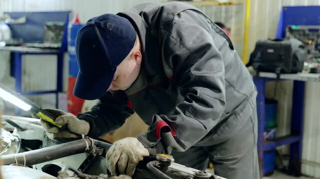 Professional mechanic wearing grey uniform, fixing windshield with specialized tools inside modern garage workshop, performing precise automotive maintenance and repair work