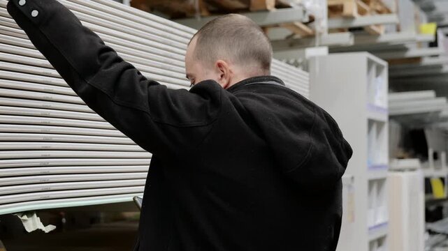 Warehouse worker checking inventory on smartphone while standing near stacked plasterboard sheets inside industrial storage facility
