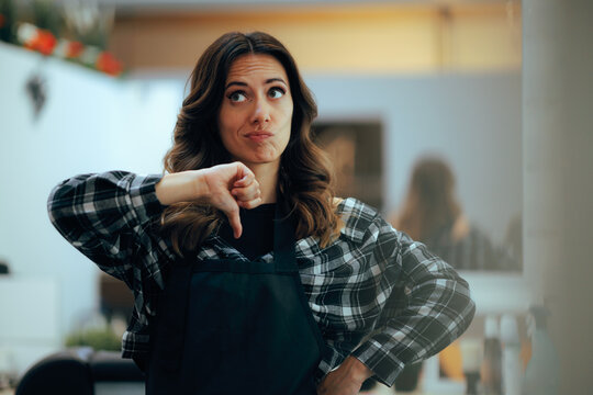 Disappointed Hairdresser Pointing down Inside her Empty Modern Salon. An unhappy salon owner stands alone looking stressed in a vacant workplace