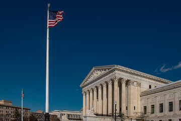 Fototapeta premium United States Supreme Court building with American flag under blue sky. Washington DC government landmark with marble columns exterior. Federal courthouse facade representing justice and law.