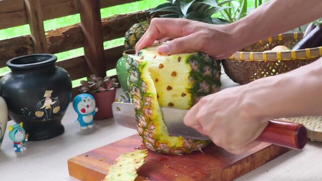 Close-up of farmer hands peeling skin of a fresh whole pineapple with sharp knife on wooden board