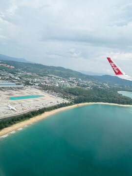 Phuket, Thailand - 5 May 2025: Aerial view of Phuket International Airport and Mai Khao beach from an airplane window with AirAsia winglet visible in the sky
