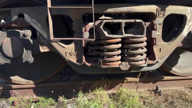 Close-up of a freight railcar bogie showing steel wheel, coil spring suspension, and cast frame on a rail siding &mdash; weathered industrial detail for logistics and engineering content