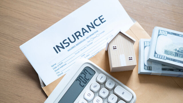 Home insurance cost calculation with calculator 2027, wooden house model, cash bundles, insurance document, and envelope on a wooden surface.