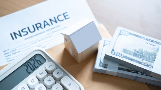 Close-up of calculator showing home expenses beside a miniature wooden house, insurance policy form, cash bundles, and envelope.