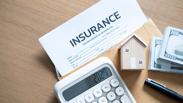 Property finance planning concept with calculator, home insurance form, miniature house, cash bundles, envelope, and black pen.