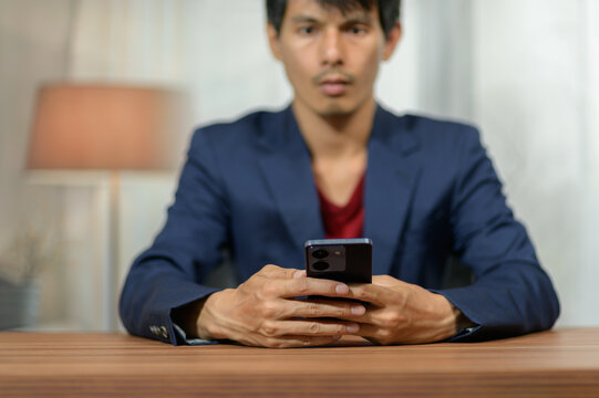Man Sitting at Desk Using Smartphone with Focused Expression in Modern Room