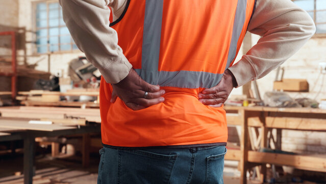 Carpenter, hands and back pain in workshop with burnout, fatigue or repetitive stress injury in industry. Project manager, tired or man in woodworking factory with physical strain or muscle stiffness