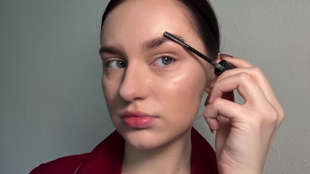 Woman applying eyebrow gel, defining her natural brows, using a spoolie brush for grooming, enhancing facial features with makeup, a daily beauty routine.
