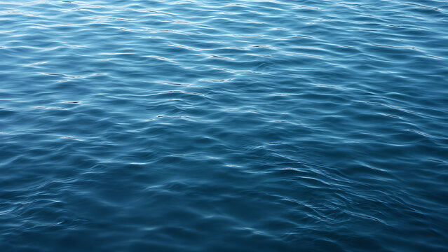 Calm blue ocean water surface with gentle rippling waves and natural sunlight texture background