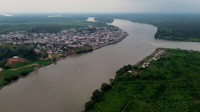 Aerial View of Riverfront Town on Wide Amazon River in Ecuador, Green Forest Banks, Rural Settlement and Remote South American Waterway Landscape
