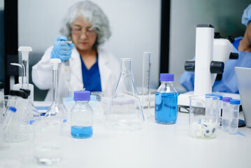 Fototapeta premium Dedicated senior Asian female scientist and her diverse laboratory team conduct advanced medical biotechnology research