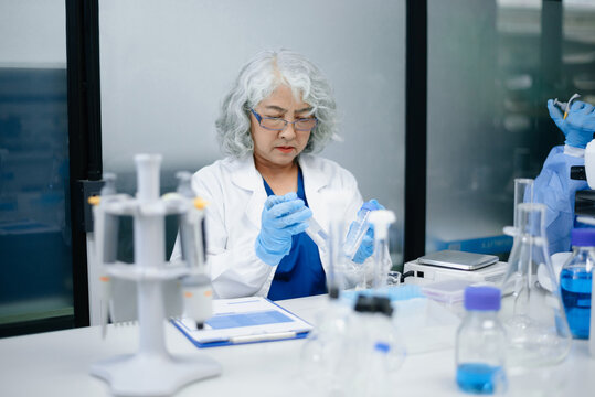 Dedicated senior Asian female scientist and her diverse laboratory team conduct advanced medical biotechnology research