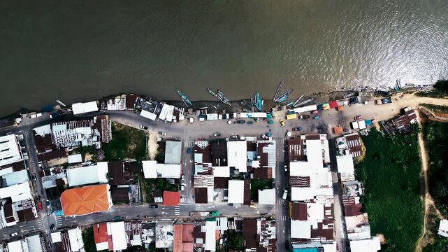 Top Down Aerial View of Amazon Riverfront Town in Ecuador with Boats, Brown Water, Shoreline Buildings and Local River Transport