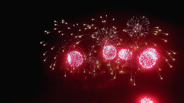 Rhythmic booms echo as brilliant crimson and white fireworks blossom high above, painting the inky Summer canvas with fleeting, fiery blooms.