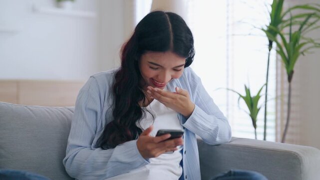 Happy young asian woman relax on comfortable couch at home texting messaging on smartphone, smiling girl use cellphone, chatting online message, shopping online from home