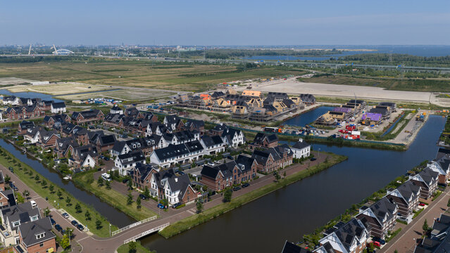 Weesp, Noord-Holland, Netherlands - 16 June 2026: Aerial view of a modern residential neighborhood with canals, dark-roofed houses, and an active construction site under a clear sky.