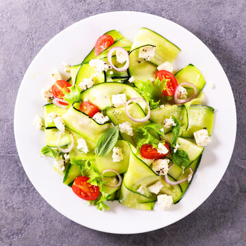 top view of zucchini ribbon salad with feta cheese tomato and onion on white plate