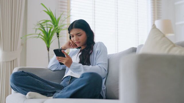 Happy young asian woman relax on comfortable couch at home texting messaging on smartphone, smiling girl use cellphone, chatting online message, shopping online from home
