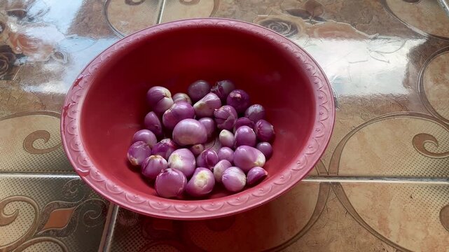Peeled red shallots in red plastic bowl food preparation close up
