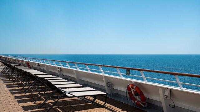Empty lounge chairs on a sunny cruise ship deck with ocean view.