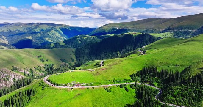 Aerial view of a winding asphalt road through lush green mountain pastures and hills with nomad tents on the Duku Highway, Xinjiang, China