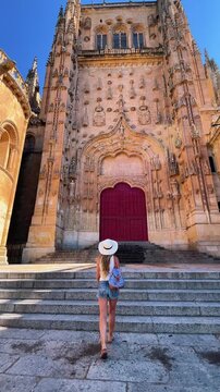 Woman in hat walking up steps to Salamanca cathedral red door in Spain