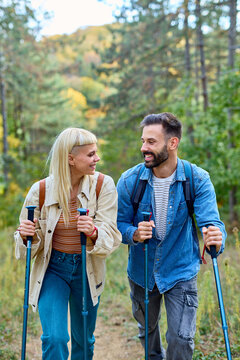 Hiking couple, young man and woman enjoys nature with trekking poles in a lush forest during a sunny day