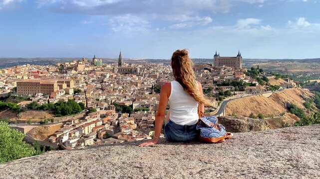 Woman sitting on rock looking at Toledo city panorama in Spain