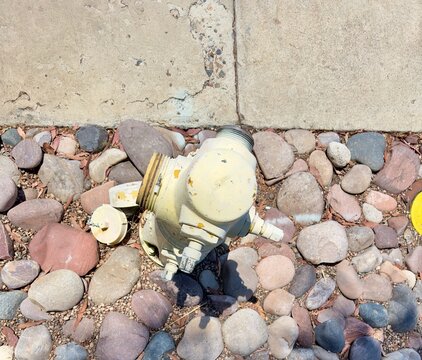 High-angle, overhead perspective of a weathered, faded yellow fire hydrant situated among river rocks in San Marcos, California.