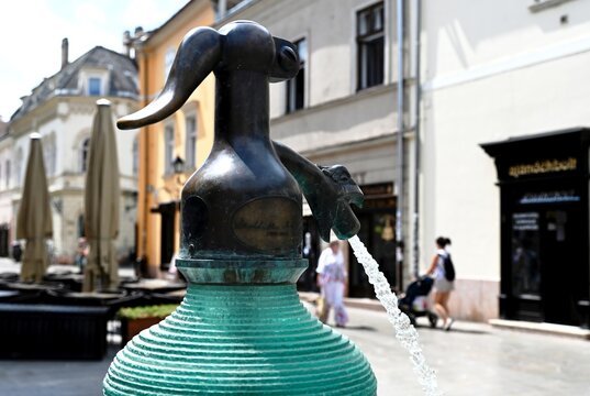 soda syphon bottle sculpture and fountain in public square. streetscape in Gyor, Hungary. layered green glass in shallow blue pool. popular landmark. outdoors, travel, tourism concept. people walking 