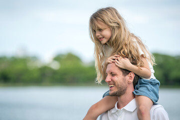 Fototapeta premium Shoulder ride with father and daughter bonding happiness family moment outdoor. Smiling father carrying daughter on shoulders walking in Park Fun Time and Active Parent Child