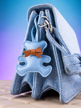 Close-up of a leather bear-shaped bag charm with a bow and loop on a blue  bag. Cute and charming accessory.