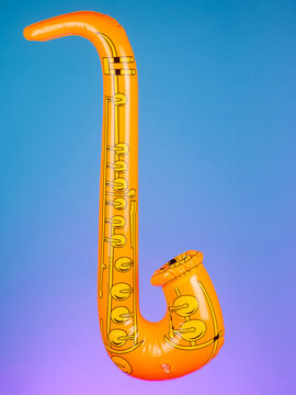 Close-up of a blow-up toy shaped like a saxophone on a purple background, highlighting its bright colors and playful design.