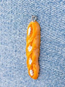 Close-up of a bread roll-shaped pendant for jewelry making, displayed on a blue background