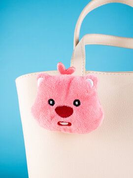 Close-up of a cute, soft bear-shaped keychain  on a  white bag.. Elegant and charming accessory