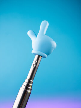 Close-up of a metallic pointer in the shape of a hand with the index finger on a blue background