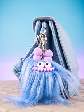 Close-up of a soft monster-shaped keychain with eyes and antennae on a  blue bag. Elegant and charming accessory.
