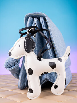 Close-up of a leather Dalmatian-shaped keychain on a  blue bag. Elegant and charming accessory