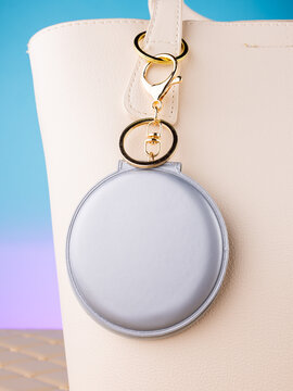 Close-up of a leather mirror-shaped keychain on a  white bag. Elegant and charming accessory.