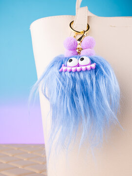 Close-up of a soft monster-shaped keychain with eyes and antennae on a  white bag. Elegant and charming accessory.