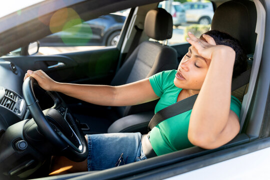 Latina woman feeling exhausted while driving car, experiencing fatigue and stress in vehicle